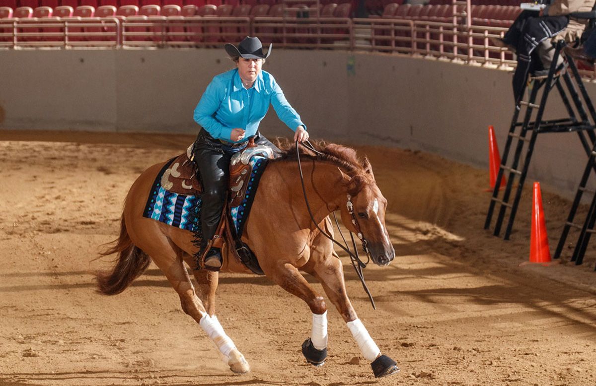 close up of horse's rear legs making a fast turn and throwing up dirt. western saddle and rider partially visible