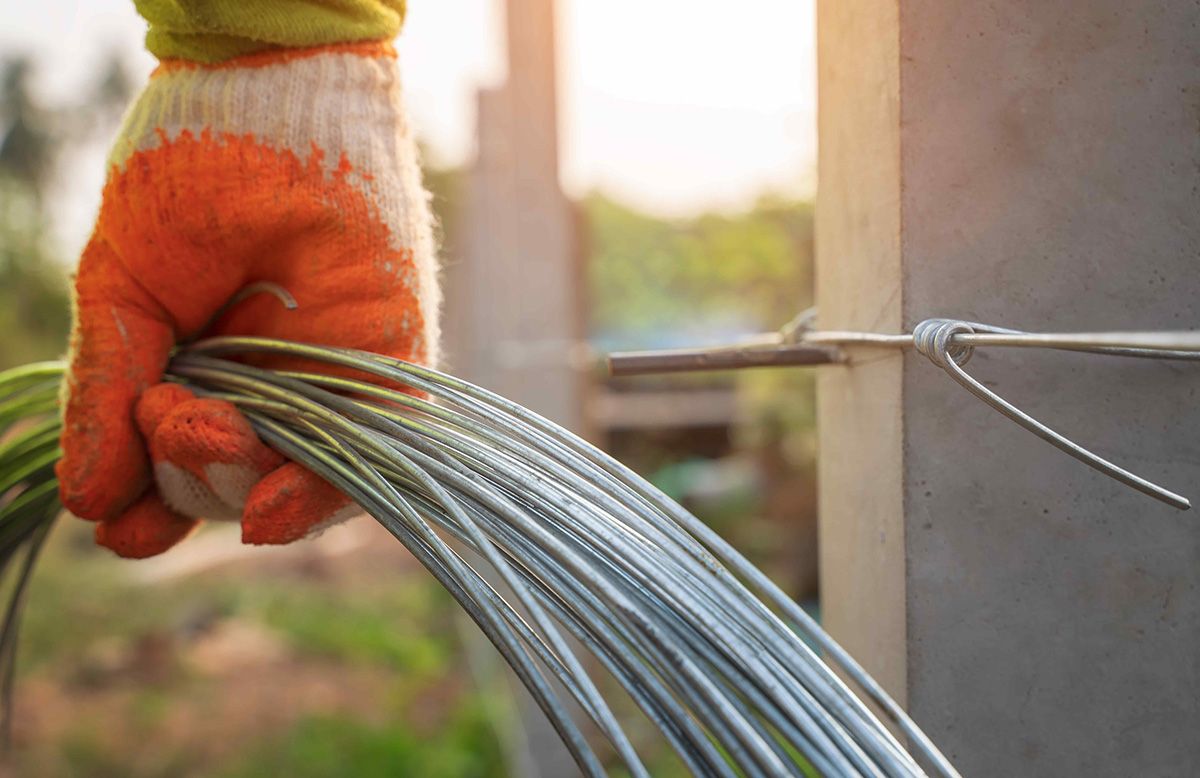 gloved hand holding coils of heavy duty wire with blurred farmland in background